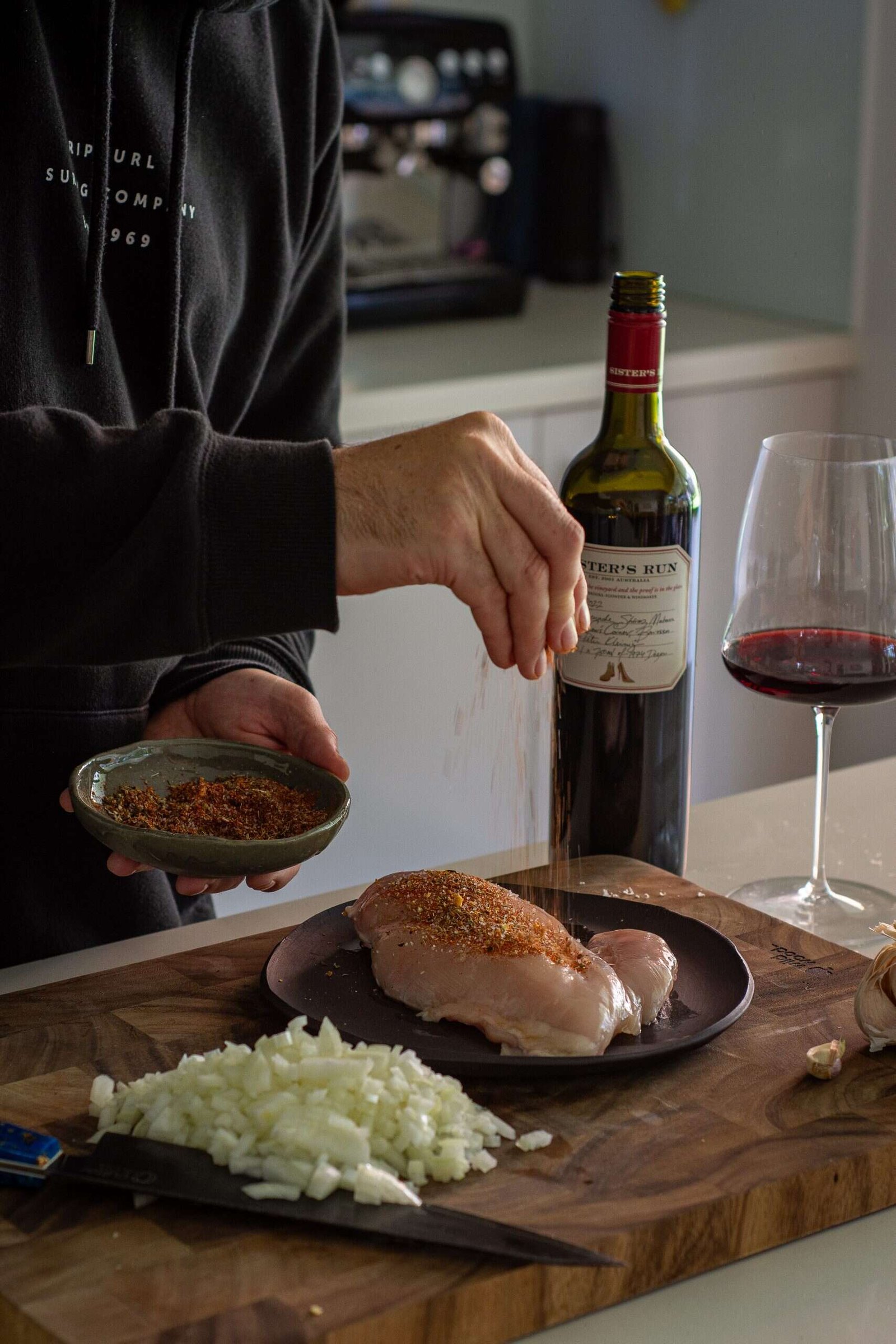 AnotherFoodBlogger seasoning chicken with a bottle of wine in background and chopped onions on board