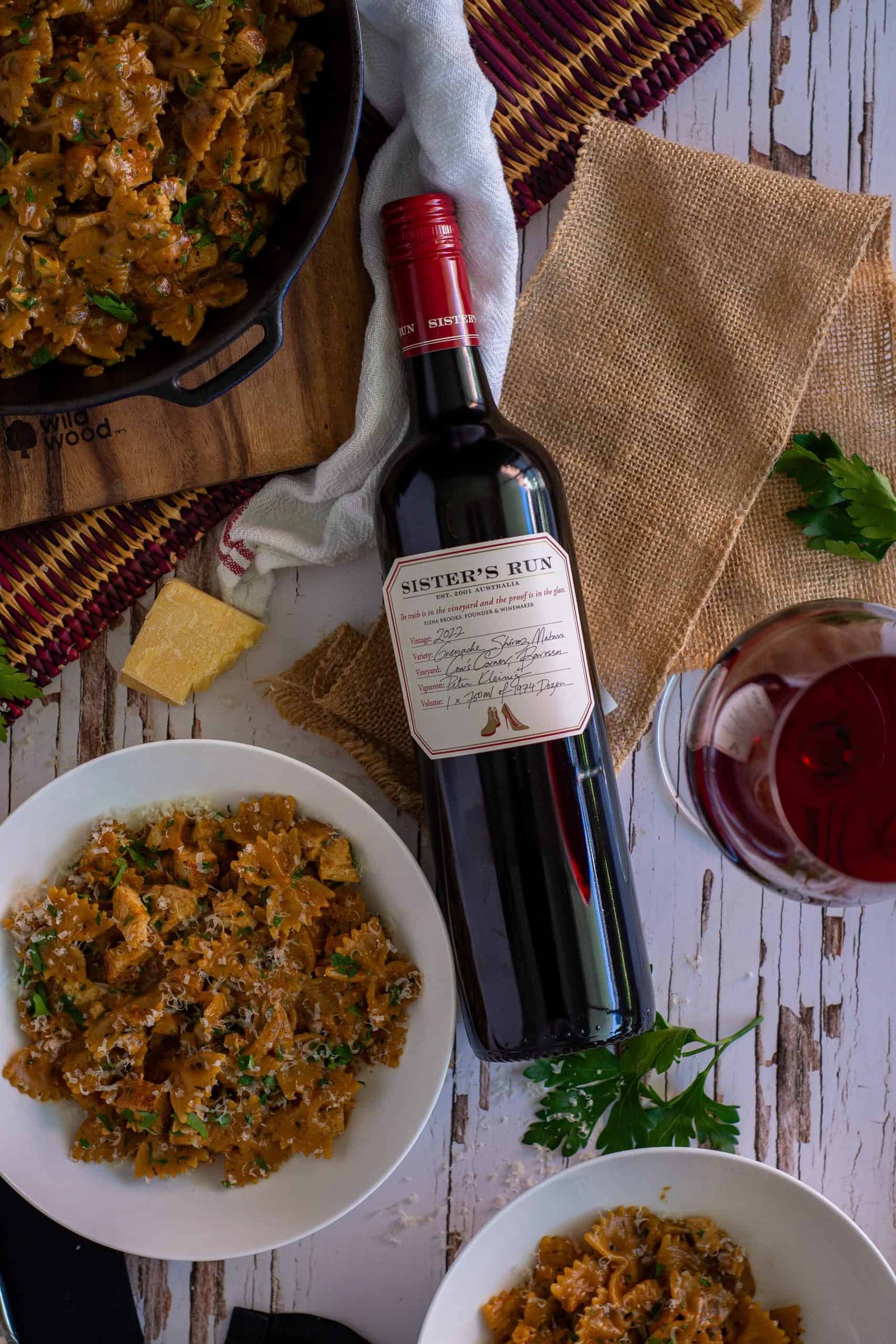 Birdseye view of blackened chicken pasta in bowls with a bottle of sisters run grenache beside them