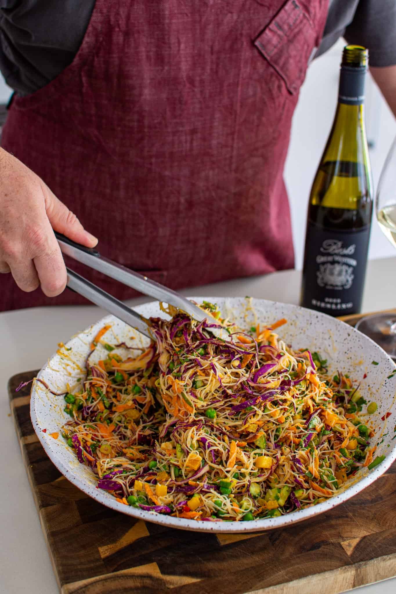 someone tossing a bowl od asian noodle salad in the kitchen 