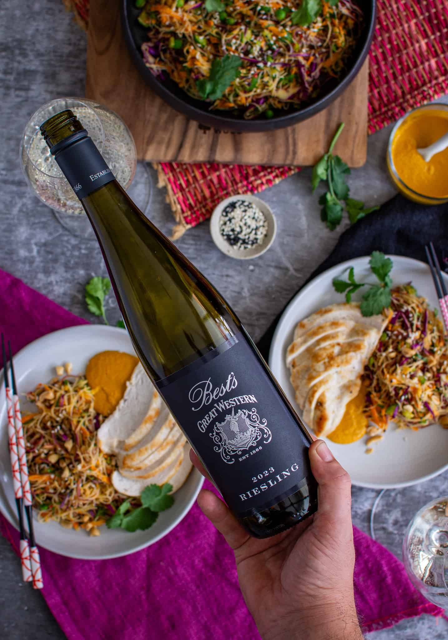 Birdseye view of someone pouring Bests Wines riesling with bowls of asian noodle salad below