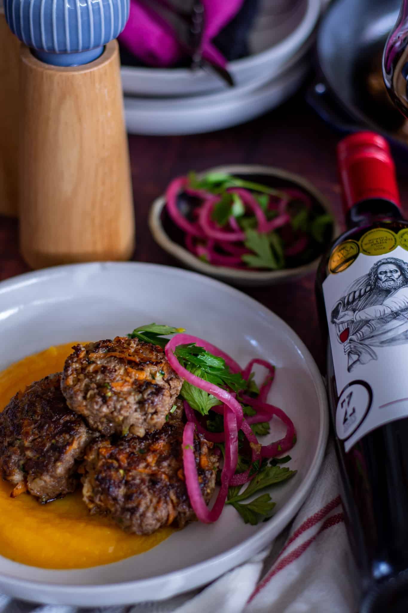 close up of beef rissoles on a plate with  a bottle of wine next to plate