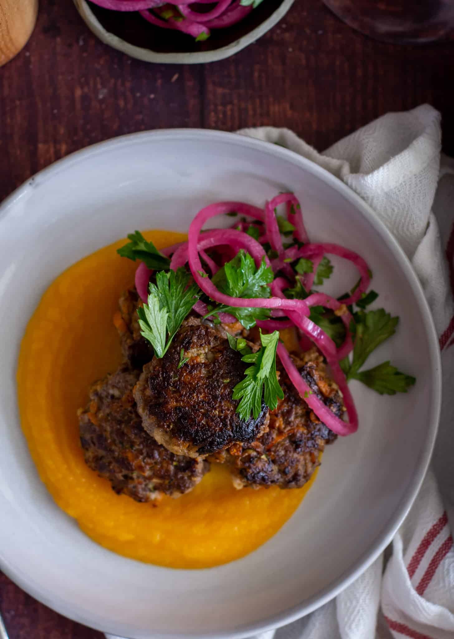close up birdseye view of beef rissoles, pumpking puree and pickled onions