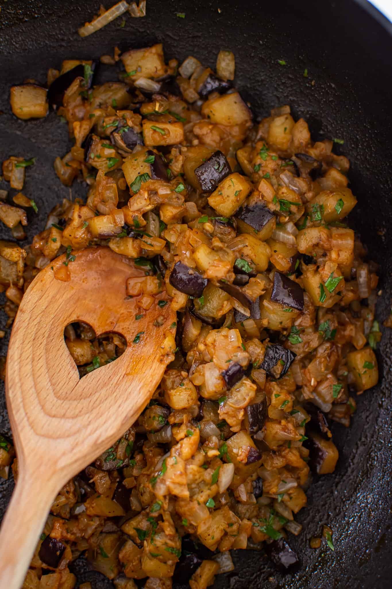 Spiced eggplant cooking in a pan with a heart shaped wooden spoon