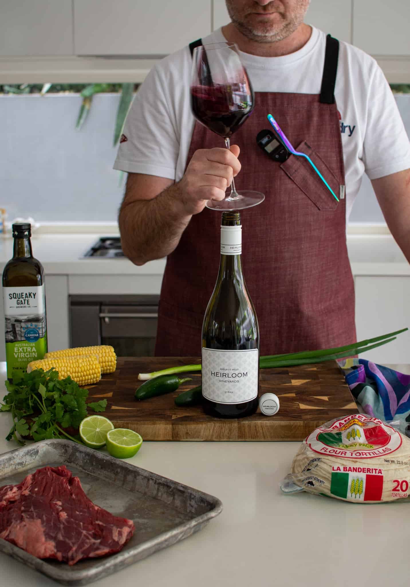 Someone swirling a glass of red wine in the kitchen with taco ingredients on the counter top 