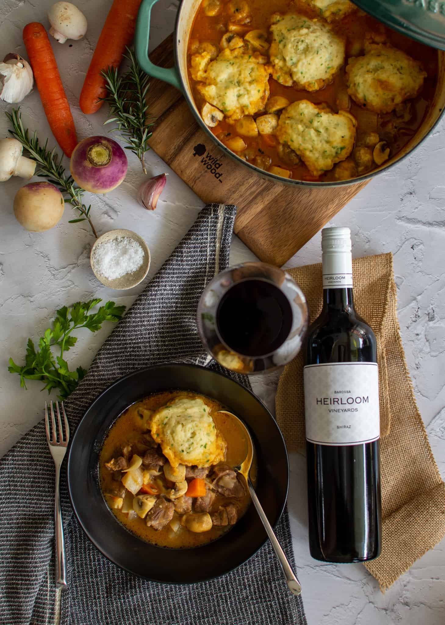 birdseye view of scottish lamb stew in a dutch oven with a black bowl of stew and a glass of heirloom shiraz next to it.