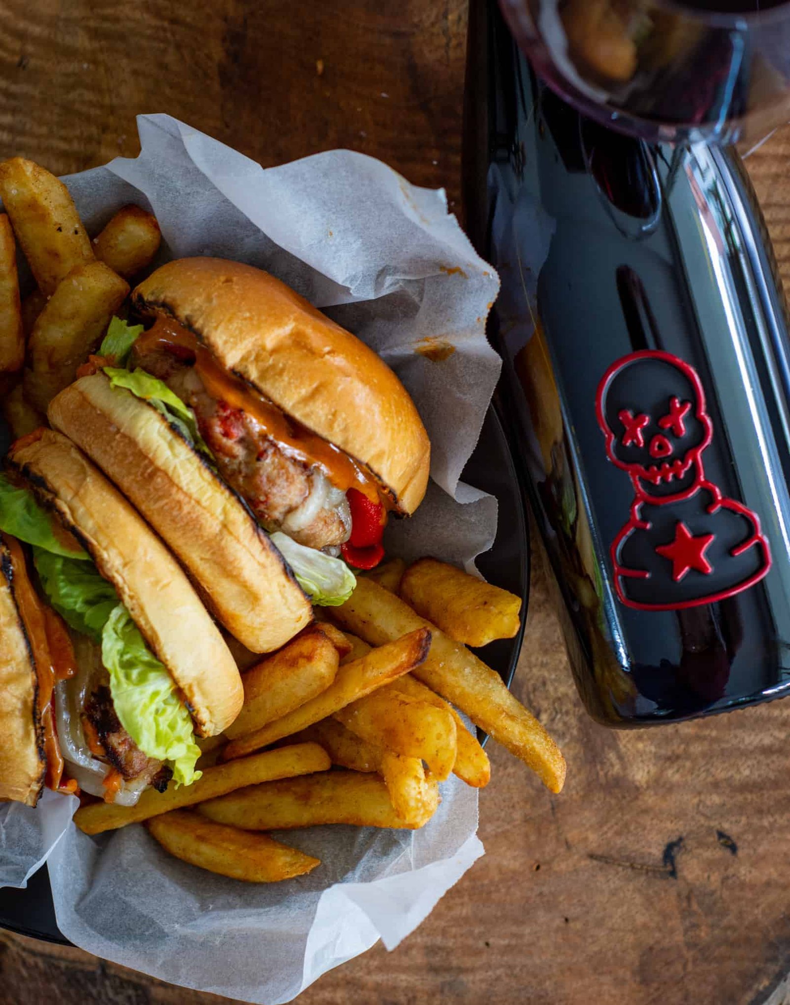 Birdseye view of a couple spanish style burgers, fries and a bottle of Pawn Wine Co Maturana Tinta