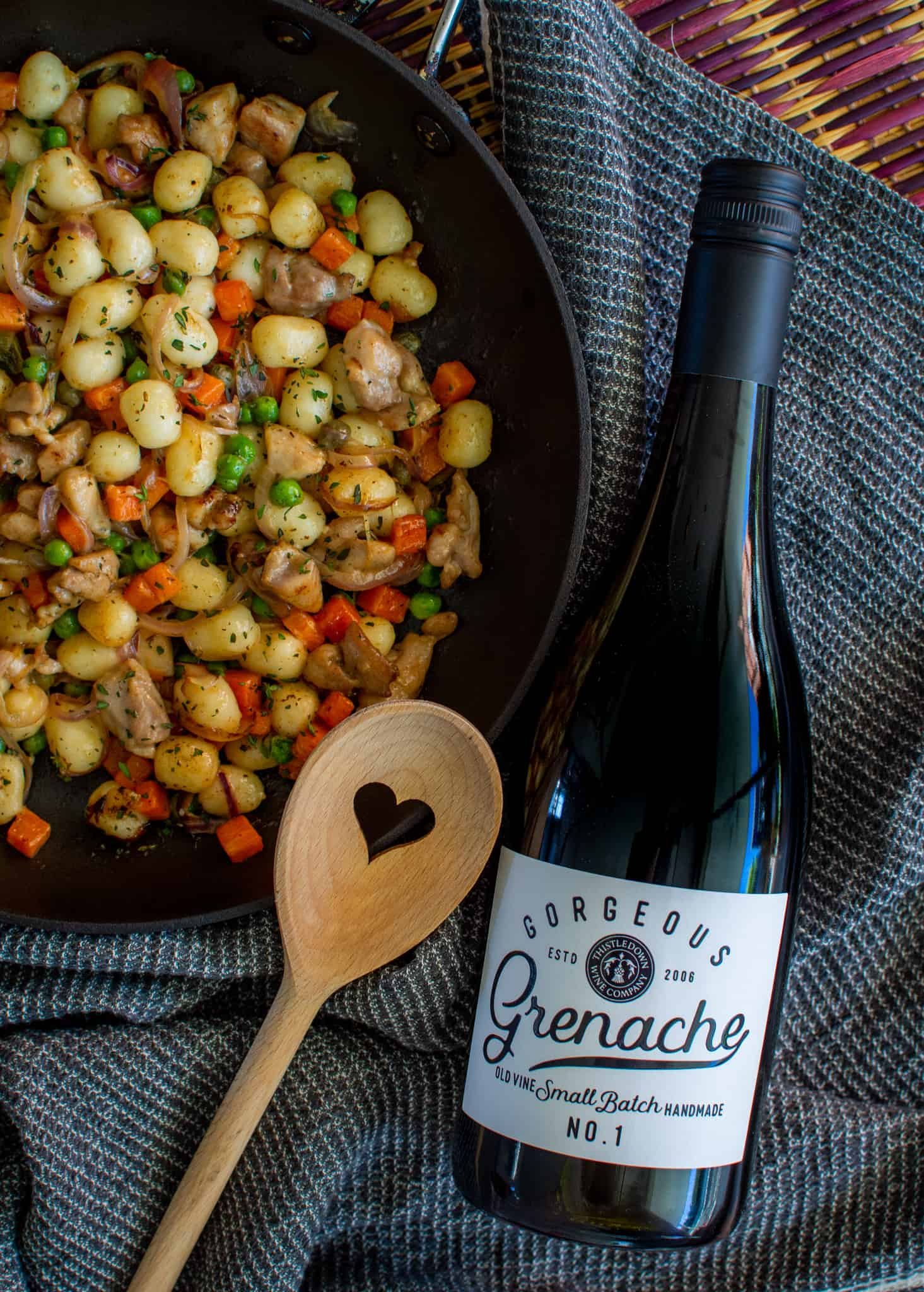 frying pan with chicken gnocchi in it, a bottle of grenache beside it and a hear shaped wooden spoon