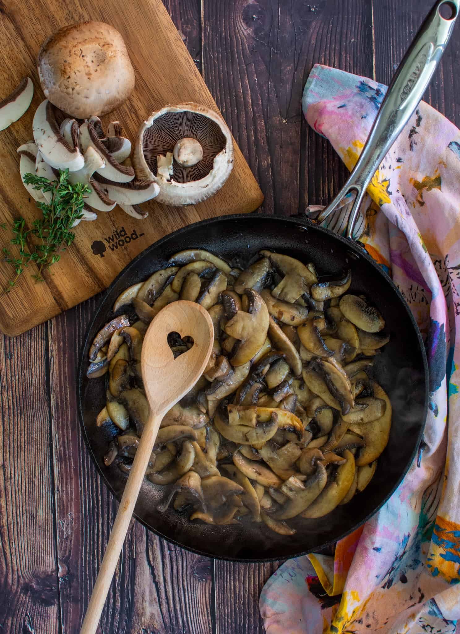 mushrooms in a frying pan with chopping board beside with mushrooms on it 