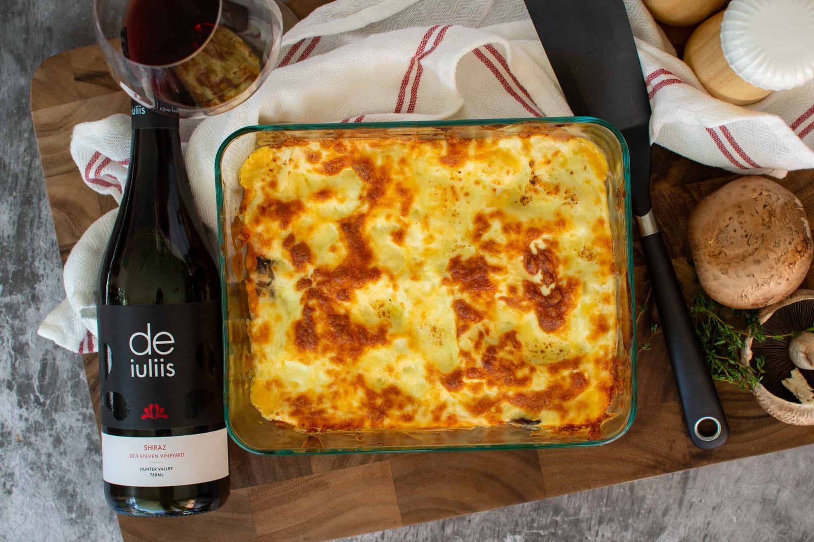 Birdeye view of vegetable lasagne in casserole dish with wine, wine glass and spatuala beside