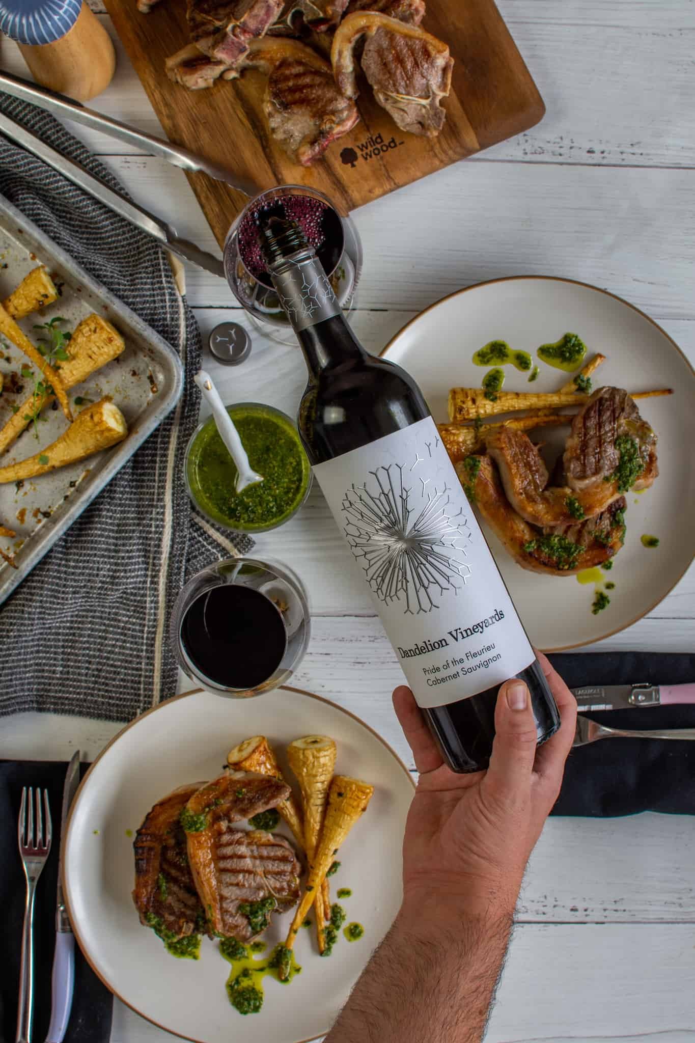 someone pouring red wine into a glass with plates of food below on a table 