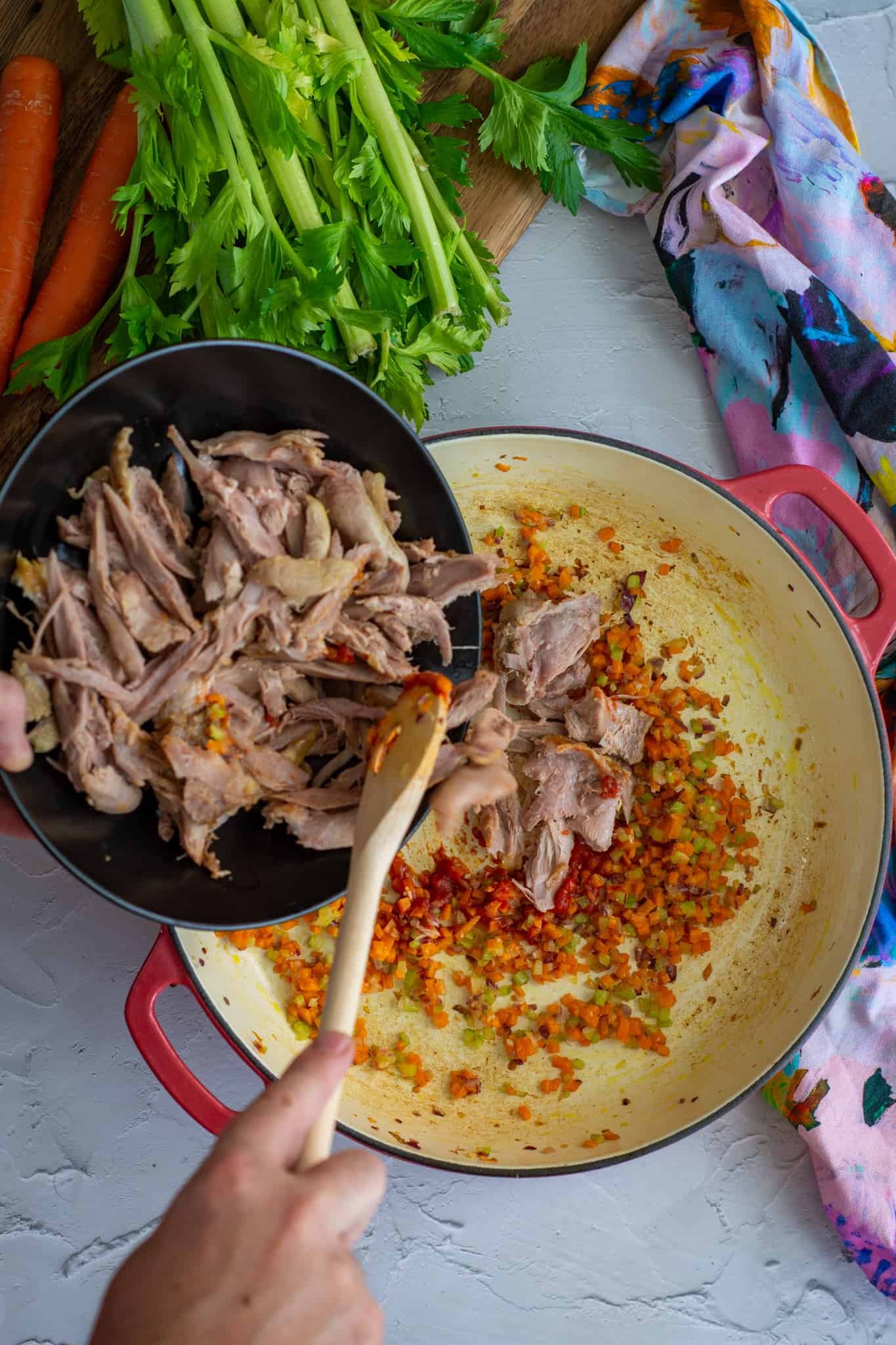 Birdseye view of someone pouring shredded duck into pan 