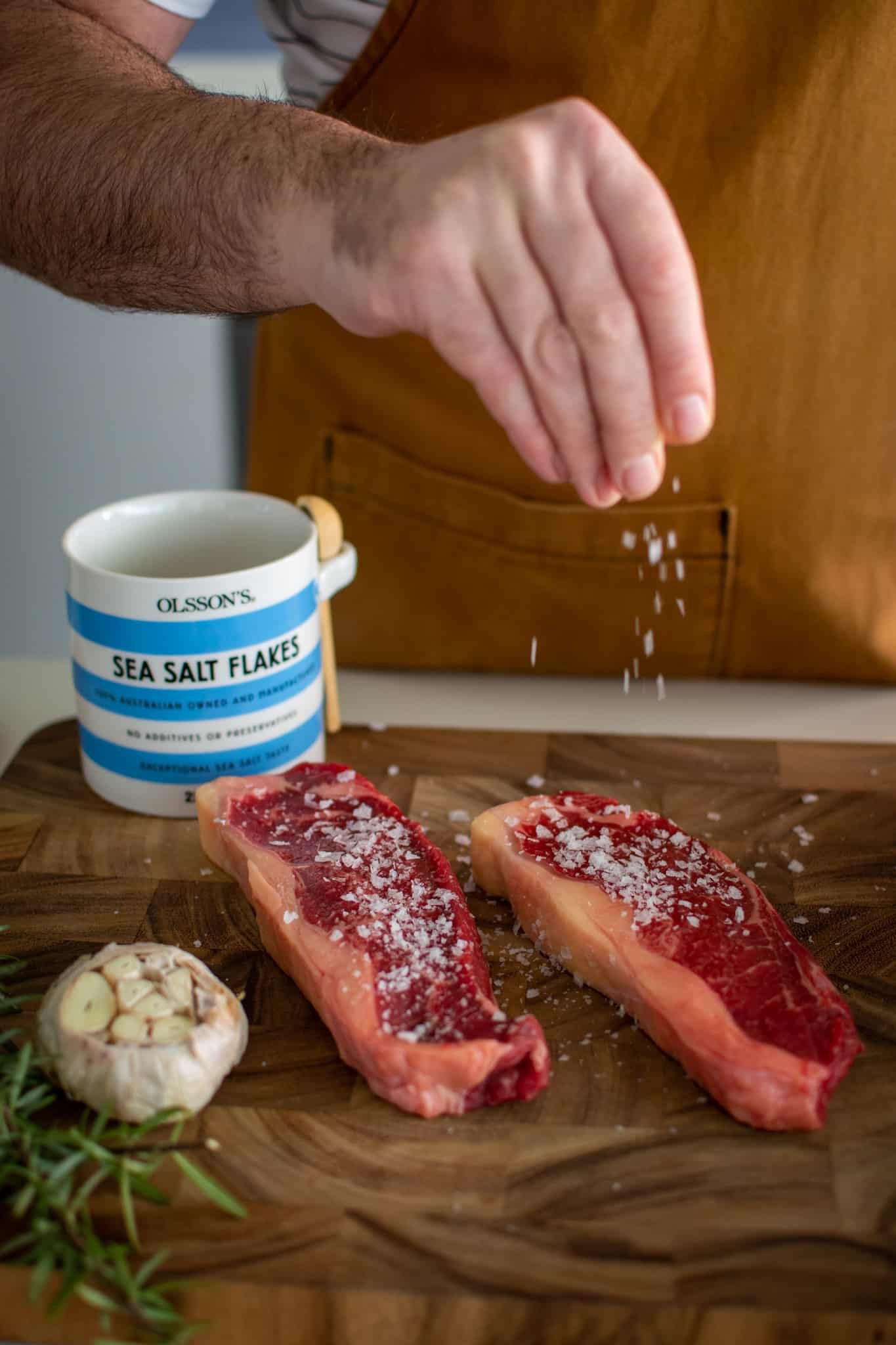 Someone seasoning steaks on a chopping board 
