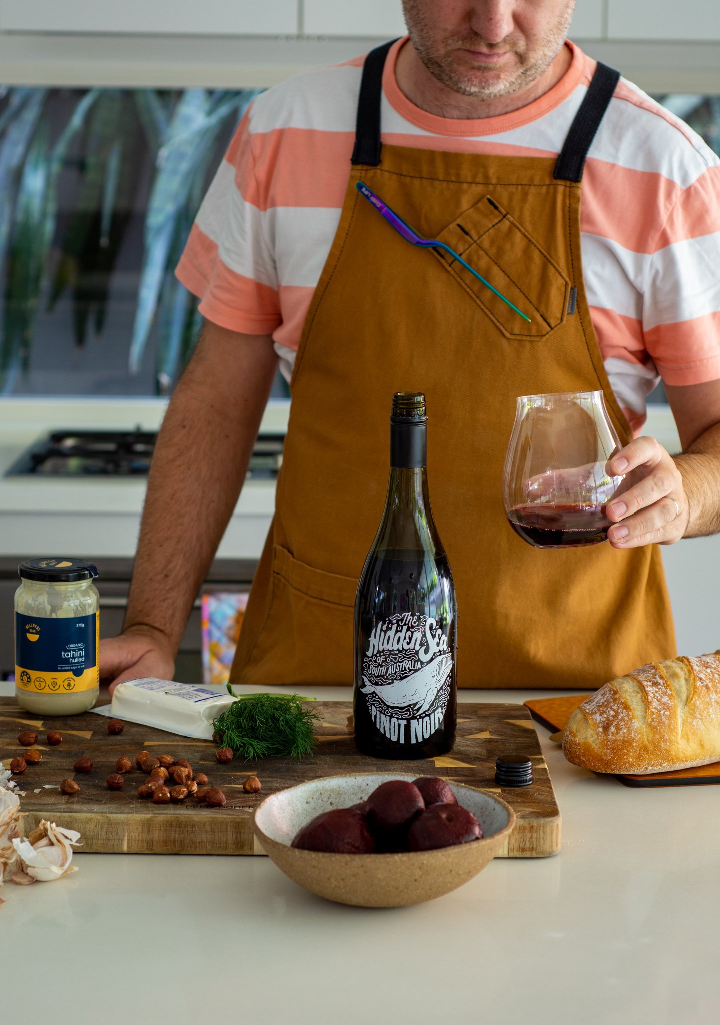 someone in the kitchen holding a glass of wine with food on counter top 
