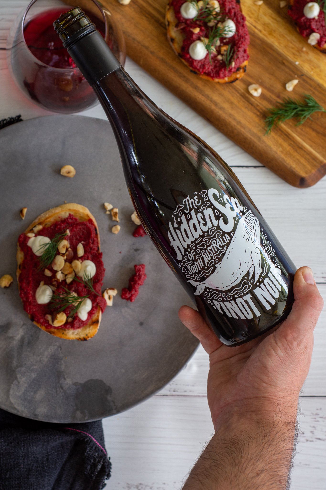 someone pouring the hidden sea pinot noir with a plate of fancy beetroot toast below 