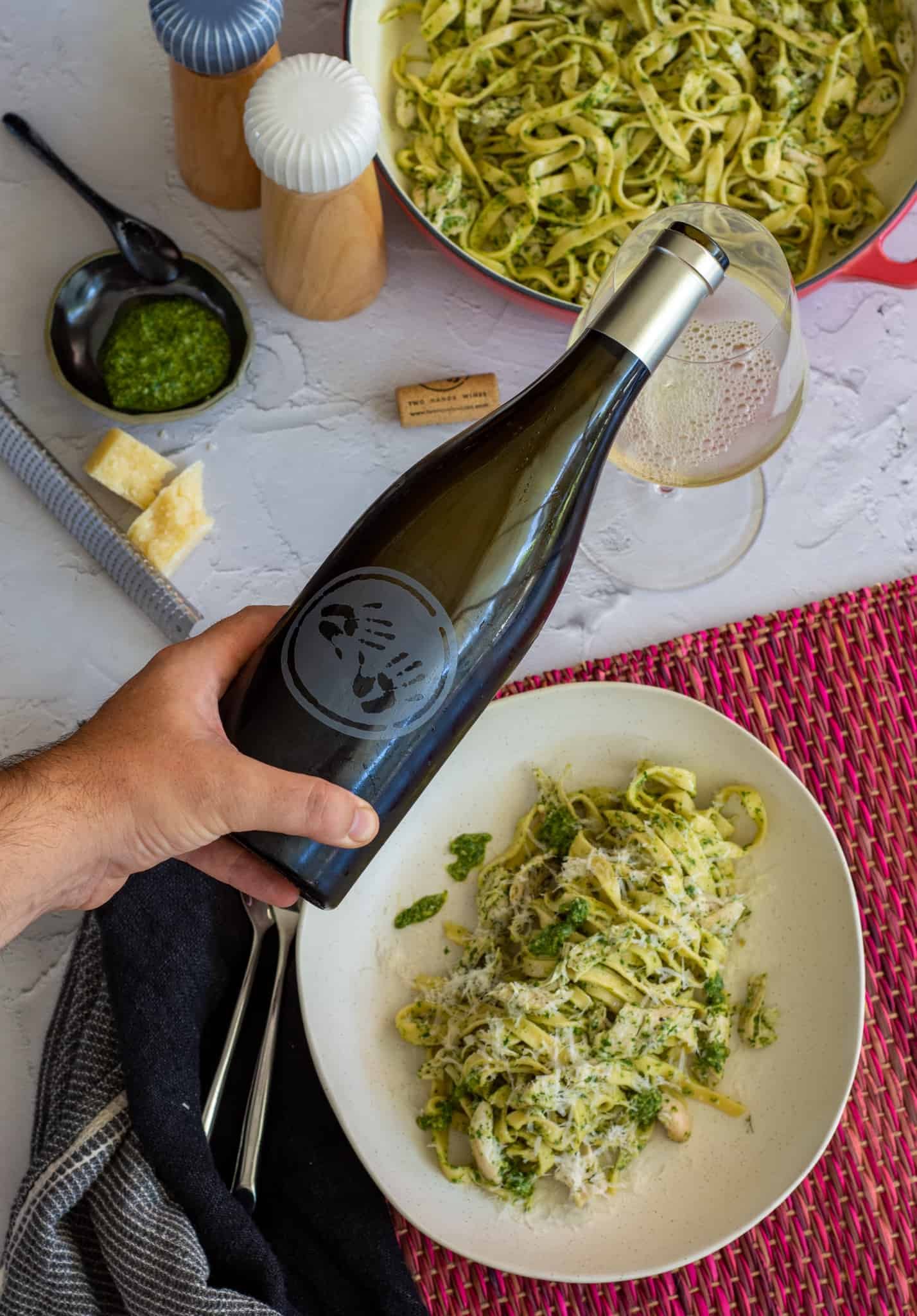 Someone pouring Two Hands chardonnay with bowls of pasta al pesto below 