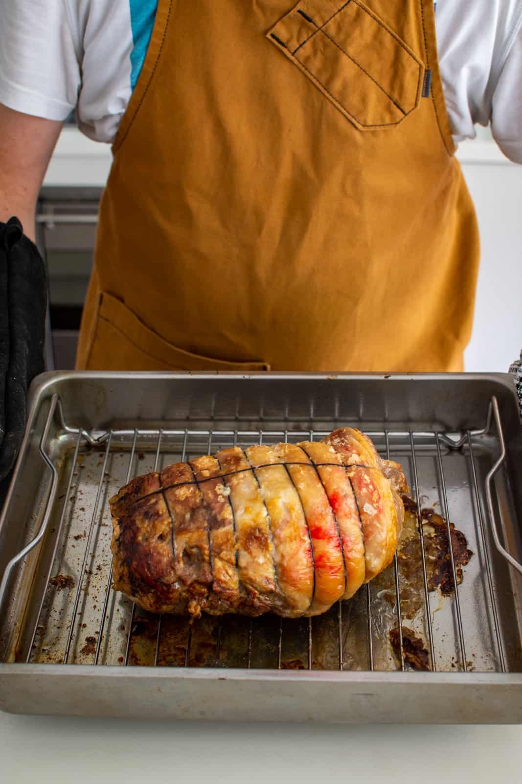 Someone holding a tray with a cooked boneless lamb leg in it 