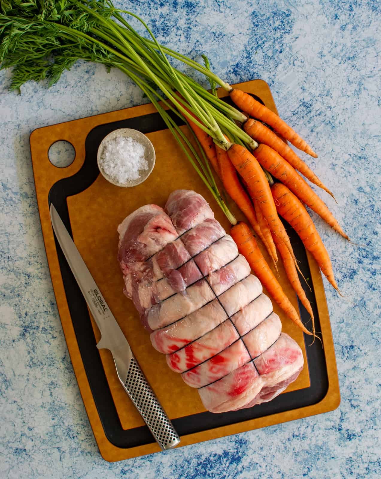 boneless lamb leg on a chopping board with a boning knife and carrots 