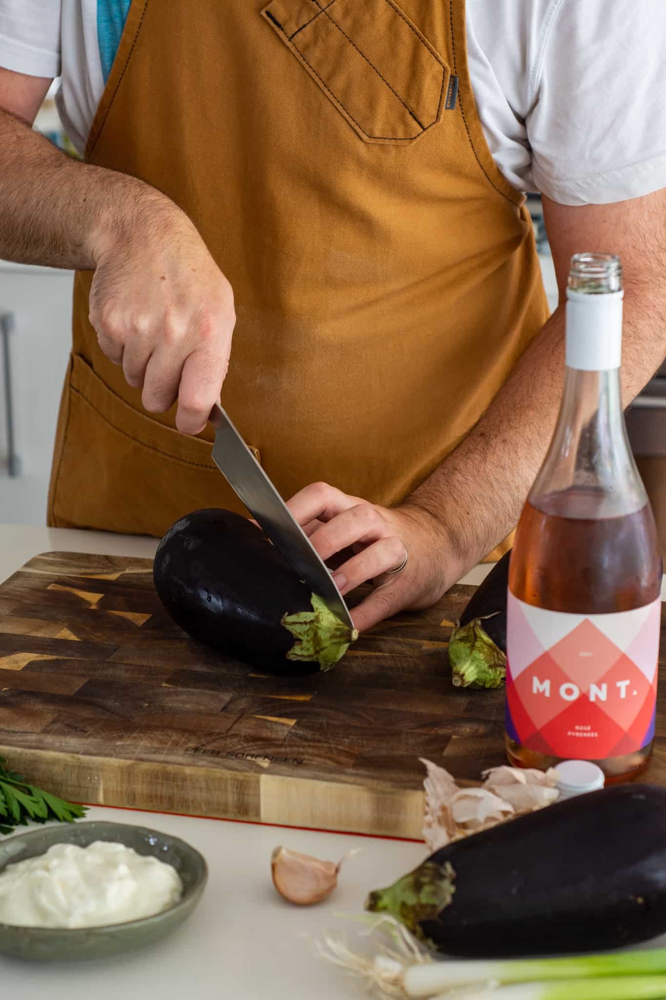 Someone is cutting eggplant on a chopping board with pink wine next to it