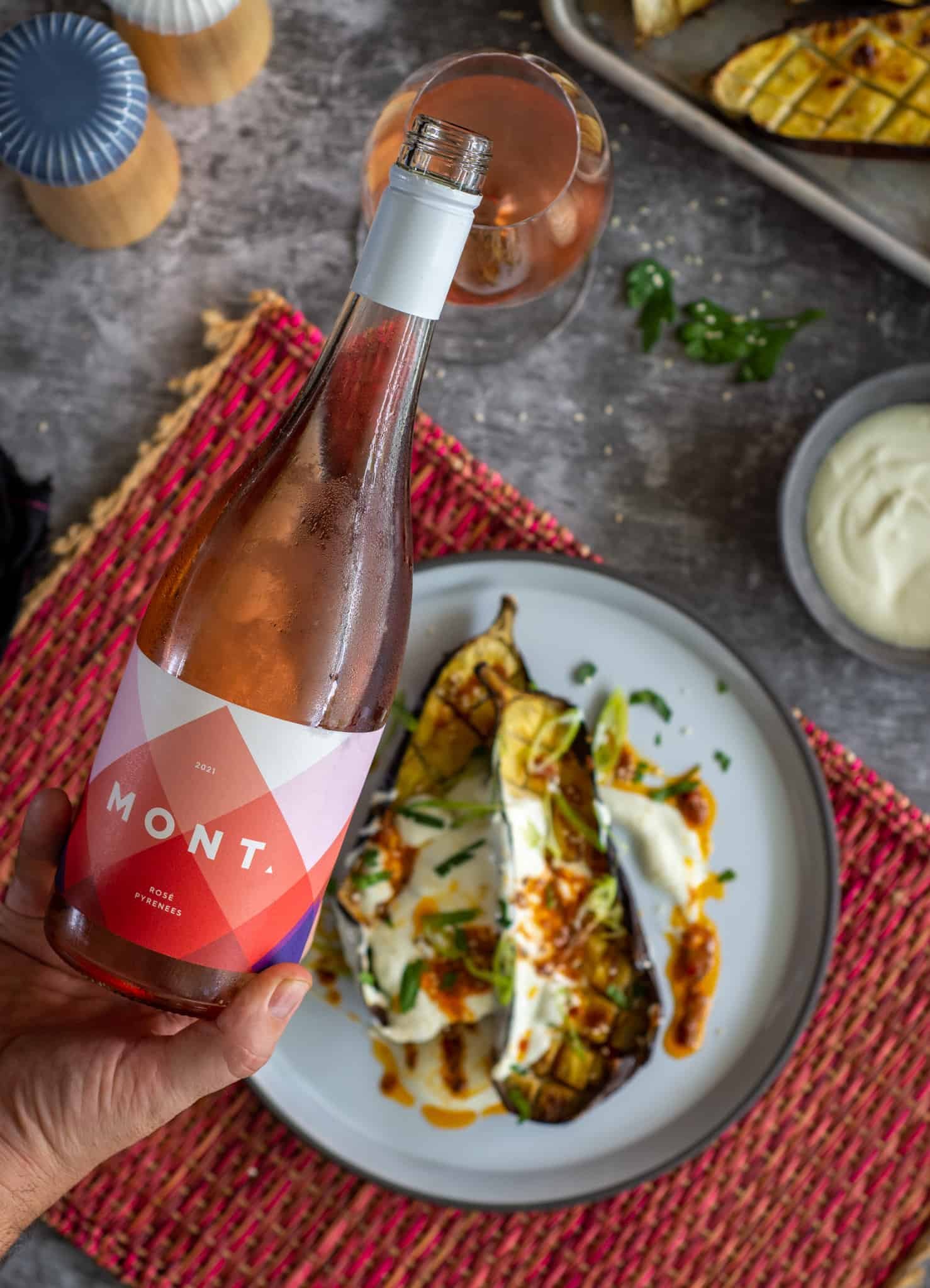 Someone is drinking a glass of rose wine with roasted eggplant and harissa butter on the plate below