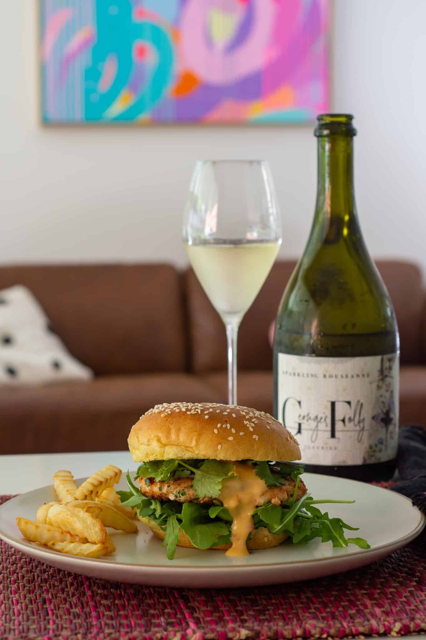 asian fish burger on a plate with sparkling wine beside.