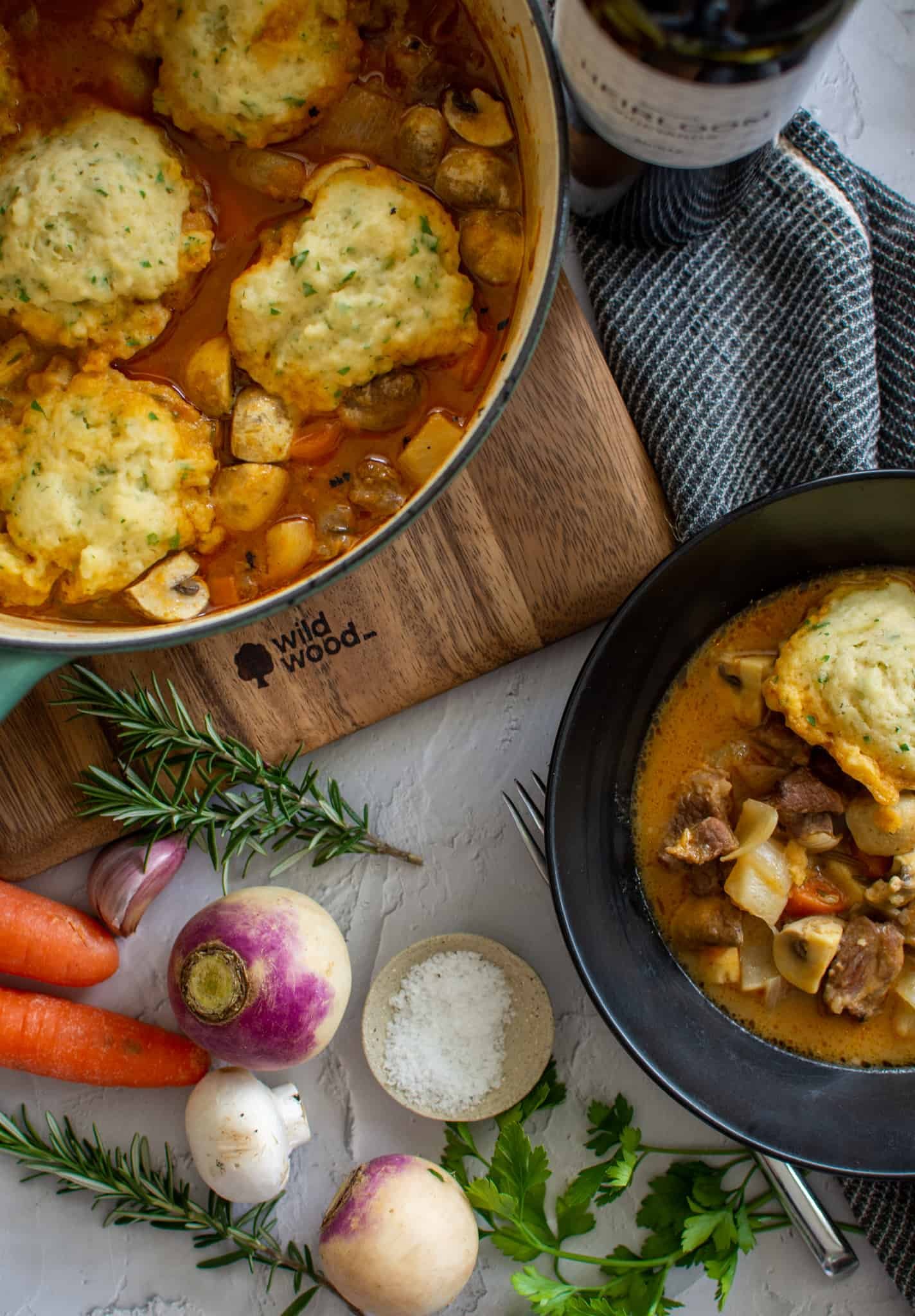 birdseye view of stew in a dutch oven and some in a smaller black bowl. vegtables are on the counter next to them 